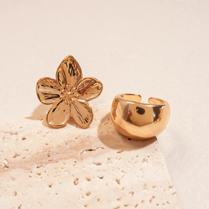 Detail of gold flower earring and smooth metallic ring on a textured stone base