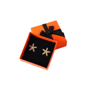 Star-shaped gold earrings with rhinestones in an orange jewelry gift box with ribbon