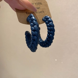 Macro detail of hand-woven navy blue leather texture on large C-shape hoop earrings