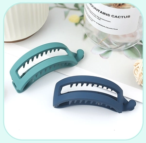 Close-up of matte dark green and blue banana hair clips on a clean white surface