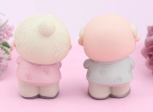 Rear view of elderly couple cake toppers in pink and grey attire on a soft pink backdrop