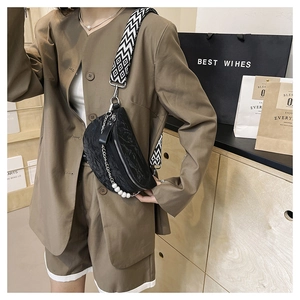 Detail of black pleated crossbody bag featuring woven strap and pearl chain accent