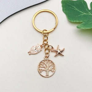 Golden keychain featuring owl, starfish, and tree of life charms on white background