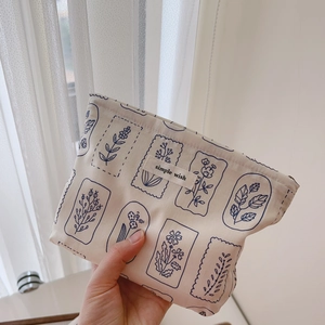 Handheld view of a beige cotton makeup bag with blue botanical prints and zip closure