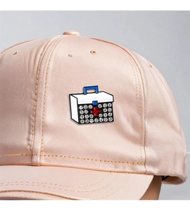 Detail of medical box enamel pin with red cross and rhinestones on a pink baseball cap