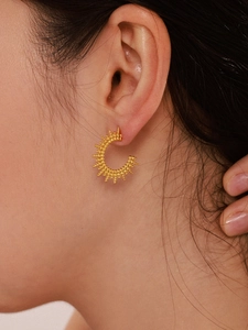 Close-up of golden C-shaped sunburst earrings with beaded texture on model ear