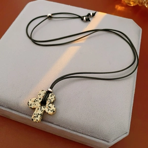 Detailed view of spotted dalmatian stone cross pendant on a black cord necklace