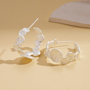 Macro detail of irregular pleated geometric C-shaped earrings in polished silver finish
