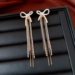 Detail of 18k gold plated bow earrings with sparkling rhinestone tassels on black leather