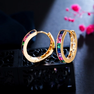 Macro shot of gold hoop earrings with multi-colored square-cut zircons on a dark stand