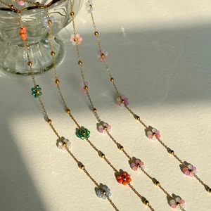 Colorful beaded flower necklaces on gold titanium steel chains draped over a glass bowl