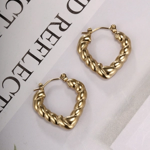 Detailed view of gold twisted rope heart hoop earrings on a fashion magazine background