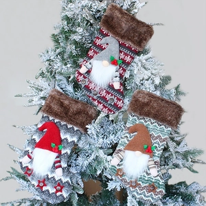 Three knitted Christmas stockings with plush gnomes hanging on a snowy Christmas tree