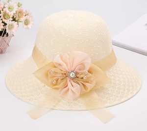 Dettaglio di un cappello in paglia crema con nastro in organza champagne e fiore di perle