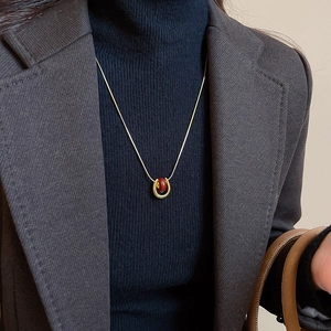 Detail of a gold plated U-shaped necklace with a red stone pendant on a blue sweater