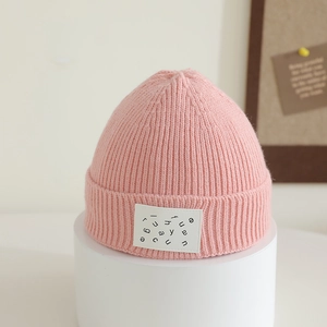 Close-up of pink ribbed knit beanie showing soft wool texture and letter patch detail