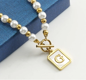 Detail view of OT buckle pearl necklace with 18K gold letter G pendant on shell base