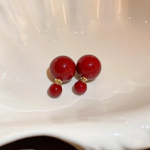 Makroaufnahme roter Doppelperlen-Ohrstecker mit Goldfinish auf einem Keramikmuschelteller