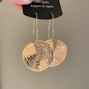 Macro detail of gold round earrings with textured spiral patterns on black card