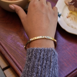 Detailed shot of gold hammered bangle with sparkling crystals worn with a grey knit sweater
