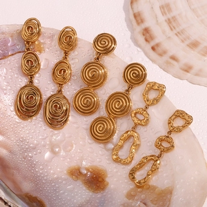 Détail de boucles d'oreilles pendantes dorées martelées sur un fond de coquillage