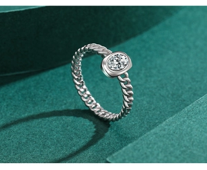 Close-up of silver chain-style ring with oval clear zircon on green background