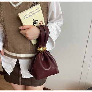 Detail of burgundy leather bucket bag with elegant gold metal ball buckle on the handle