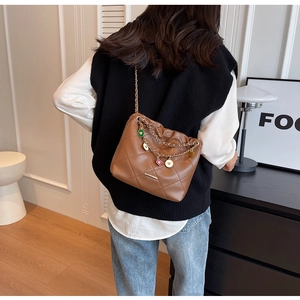 Detail view of brown quilted shoulder bag featuring gold chain strap with colorful charms