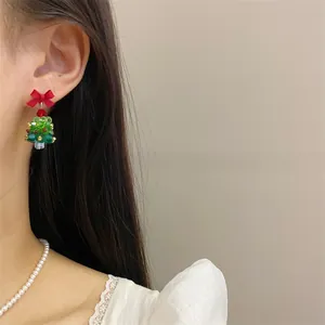Close-up of handmade beaded Christmas tree earrings with red ribbon bow on a model