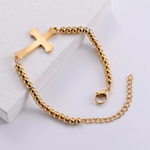 Gold titanium steel bracelet with cross charm and beads on white stone background