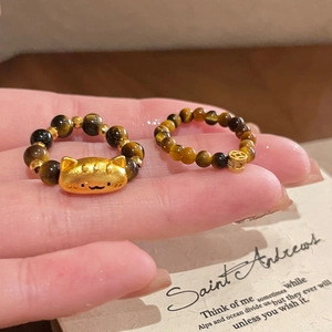 Detailed view of elastic tiger eye bead rings with cat and coin charms on fingers