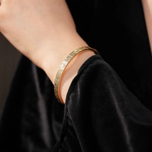 Close-up of gold mahjong texture bangle on black velvet sleeve for a stylish look