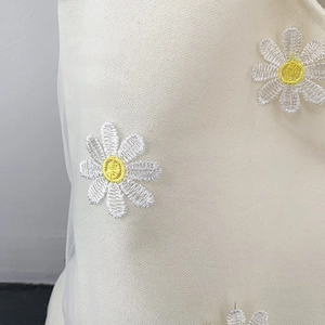 Detail of dual-layer fabric featuring white daisy embroidery over breathable mesh and canvas
