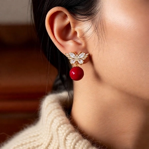 Close-up of golden butterfly earring with sparkling crystals and a glossy red drop bead