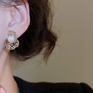 Detail of twisted hollow butterfly earrings with zircons and pearl on model's ear