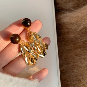Detail of amber resin bead and gold leaf tassel earrings held against a fur background