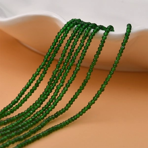 Close-up of 2mm faceted green crystal beads hanging from a white ceramic plate