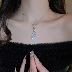 Détail du collier en Y argenté avec pierres gouttes bleu foncé sur pull noir