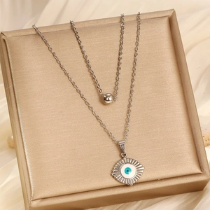 Detail of layered stainless steel necklace with blue evil eye pendant and round bead