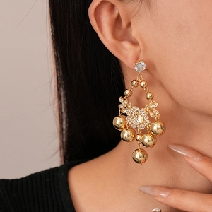 Détail de boucles d'oreilles boules dorées avec fleur en cristal portées sur l'oreille