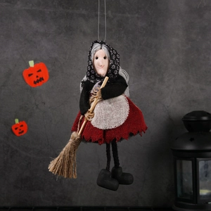 Halloween witch doll with broom and red linen skirt hanging against a grey wall