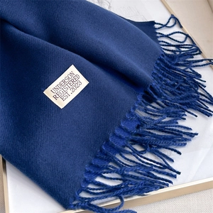 Close-up of a dark blue cashmere-feel scarf with fringes and a woven brand label