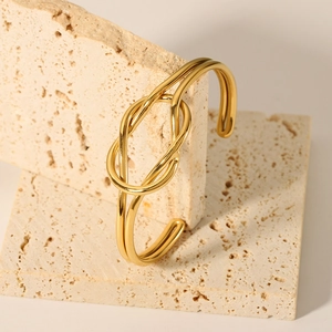 Detailed view of an 18K gold plated knotted stainless steel cuff on beige travertine stone
