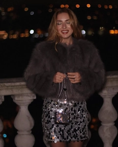 Detail of grey faux fur jacket with silver sequin skirt and black chain bag in city night