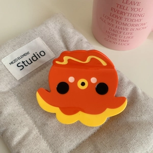 Pince à cheveux poulpe mignonne en acétate orange et jaune sur une pochette grise