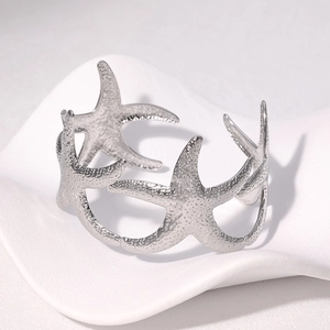Close-up of silver starfish cuff bracelet with textured details on a white ceramic tray