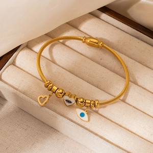 Detail of gold woven steel bracelet with heart charms and blue evil eye pendants