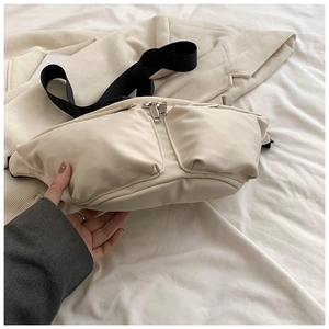 Detail view of cream nylon crossbody bag with dual front pockets and adjustable strap