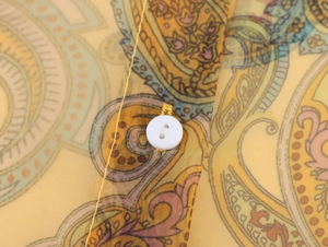 Detailed view of white four-hole button on yellow paisley chiffon organza fabric