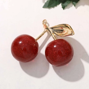 Macro shot of glittery red cherry pendant with golden leaf detail and metal hanging loop
